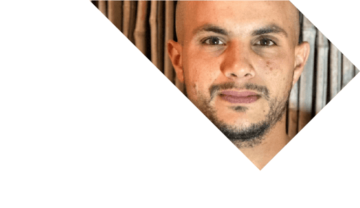 גבר עם ראש מגולח וזקן קצר נראה חלקית בתוך מסגרת משולשת, על רקע מעוטר. | DeckTech דקים, פרגולות ועבודות בנייה בעץ