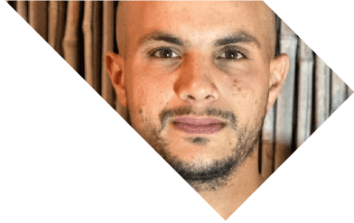 תקריב של גבר עם שיער קצר וזקן, על רקע של לוחות עץ אנכיים. התמונה מסובבת באלכסון. | DeckTech דקים, פרגולות ועבודות בנייה בעץ