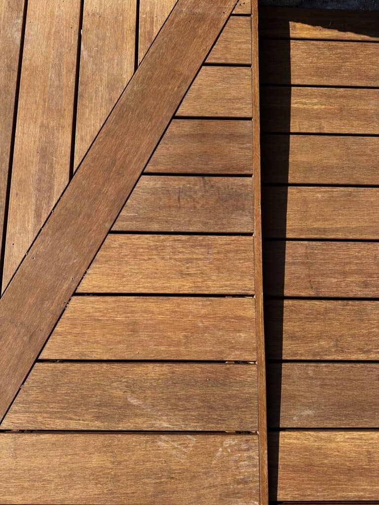 תקריב של לוחות עץ המסודרים בכיוונים שונים, היוצרים תבנית גיאומטרית עם טקסטורה גלויה וצללים המוטלים על ידי אור השמש. | DeckTech דקים, פרגולות ועבודות בנייה בעץ