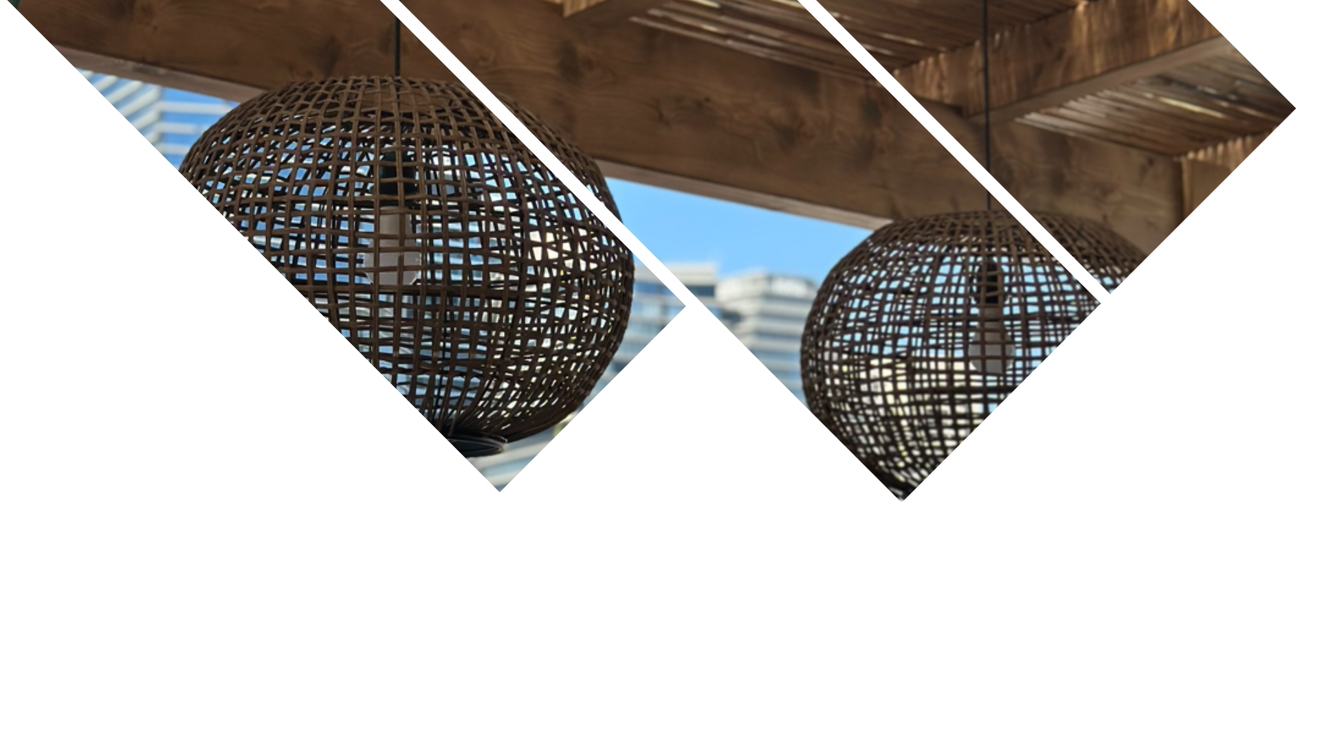 שני גופי תאורה כדוריים עשויים קש תלויים על פרגולה מעץ, כשברקע נראים שמיים כחולים ובניינים. התמונה מחולקת באלכסון לקטעים גיאומטריים. | DeckTech דקים, פרגולות ועבודות בנייה בעץ